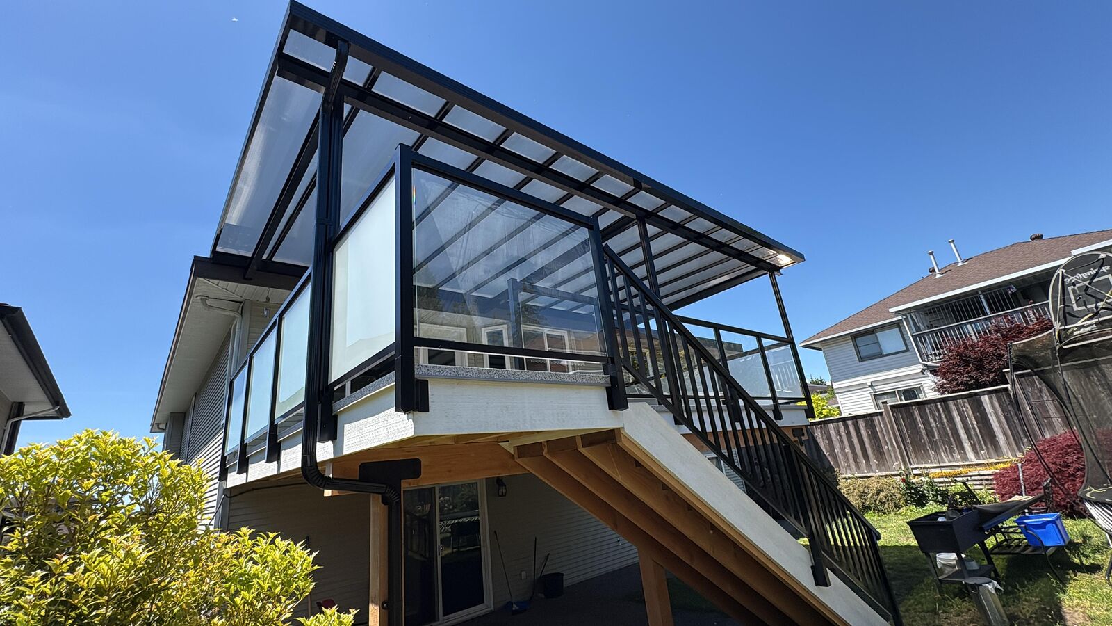 Glass deck railing under a patio cover with black aluminum stair railing on a new Cloverdale home